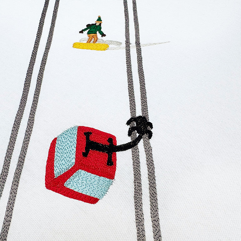 Embroidered design of a snowboarder on a snowboard with a helmet and ski pole on a white background.
