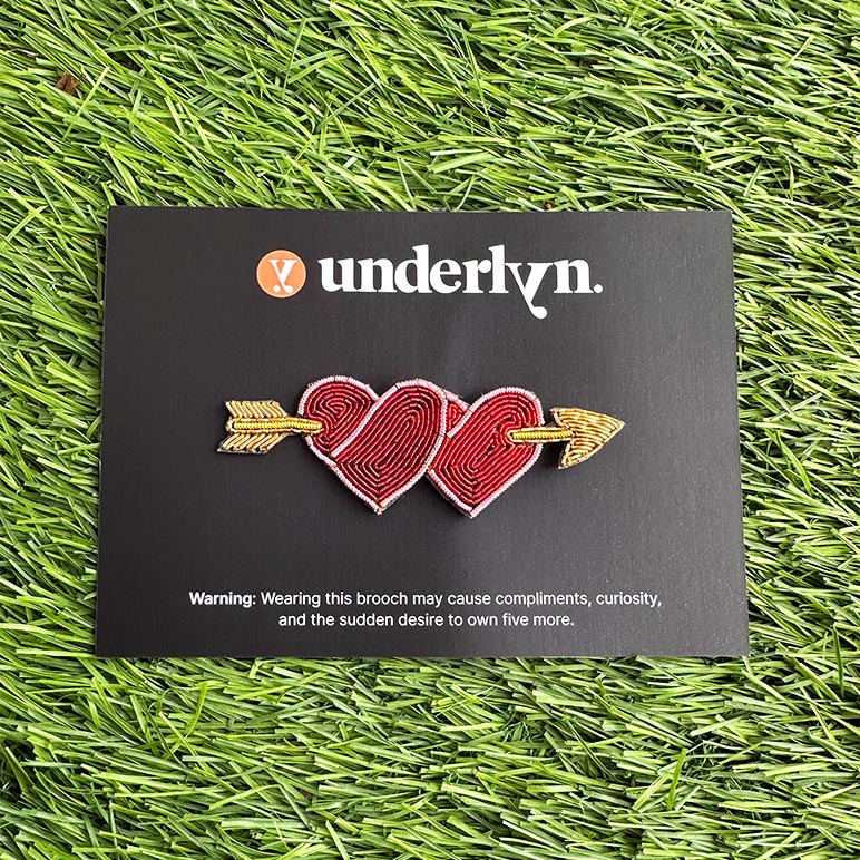 Brooch with two interlocking hearts and an arrow on a black card with &