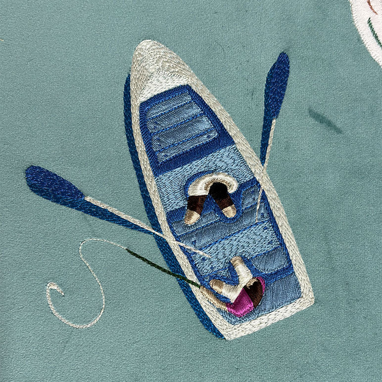 Embroidered design of a boat with a person inside on a teal background
