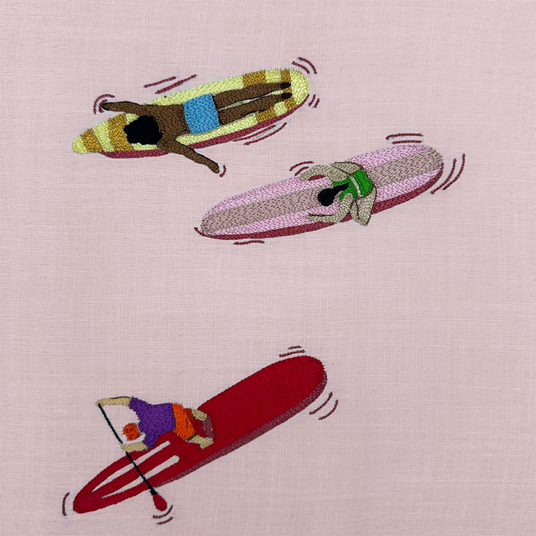 Embroidered design of three people on surfboards with a pink background