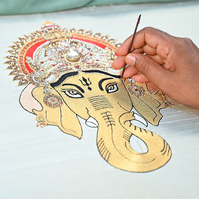 Hand painting a detailed design of an elephant head with decorative elements on a white surface.