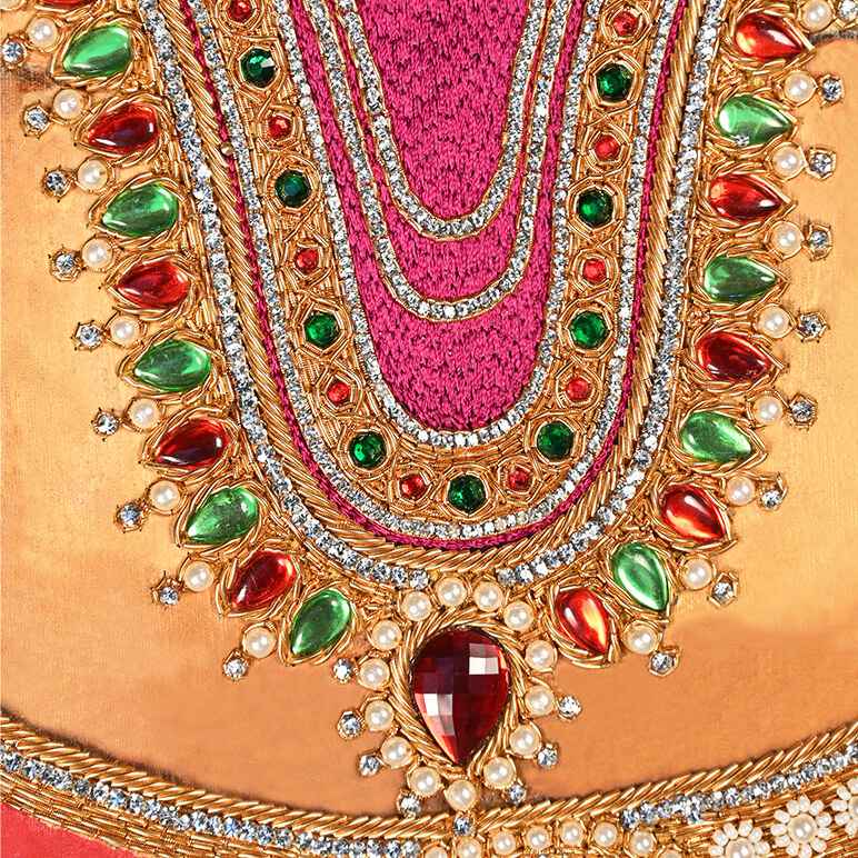 Close-up of a decorative headpiece with gold, red, and green gemstones on a pink background.