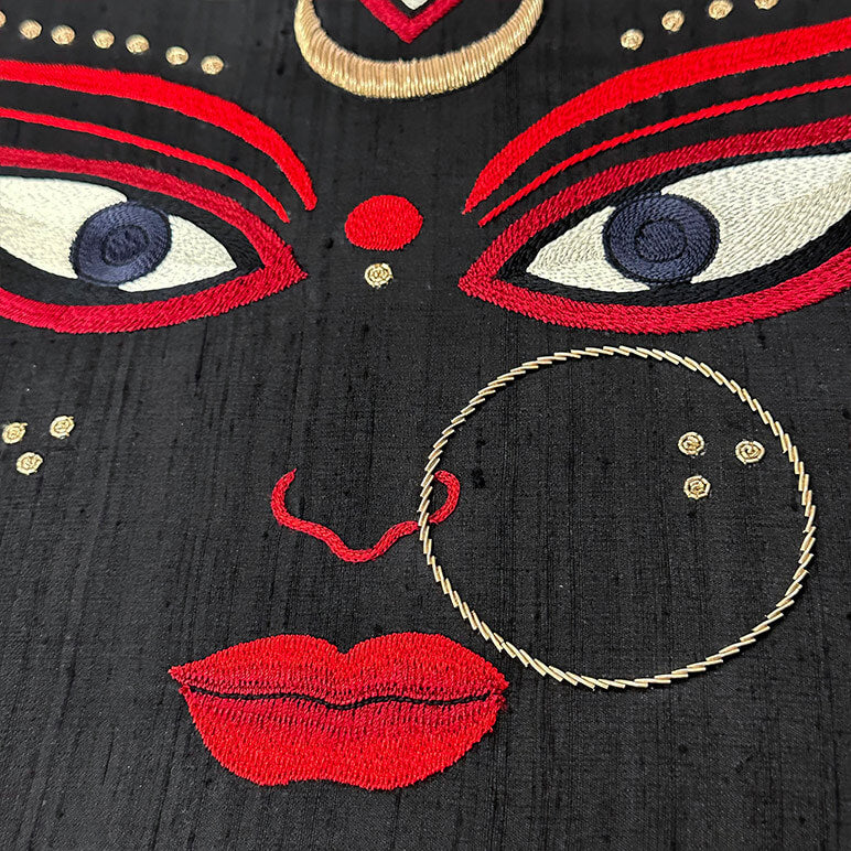 Embroidered face design with red lips, eyes, and gold accents on black fabric.