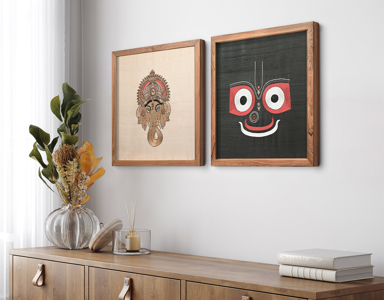 Two framed artworks on a wall above a wooden cabinet with decorative items.