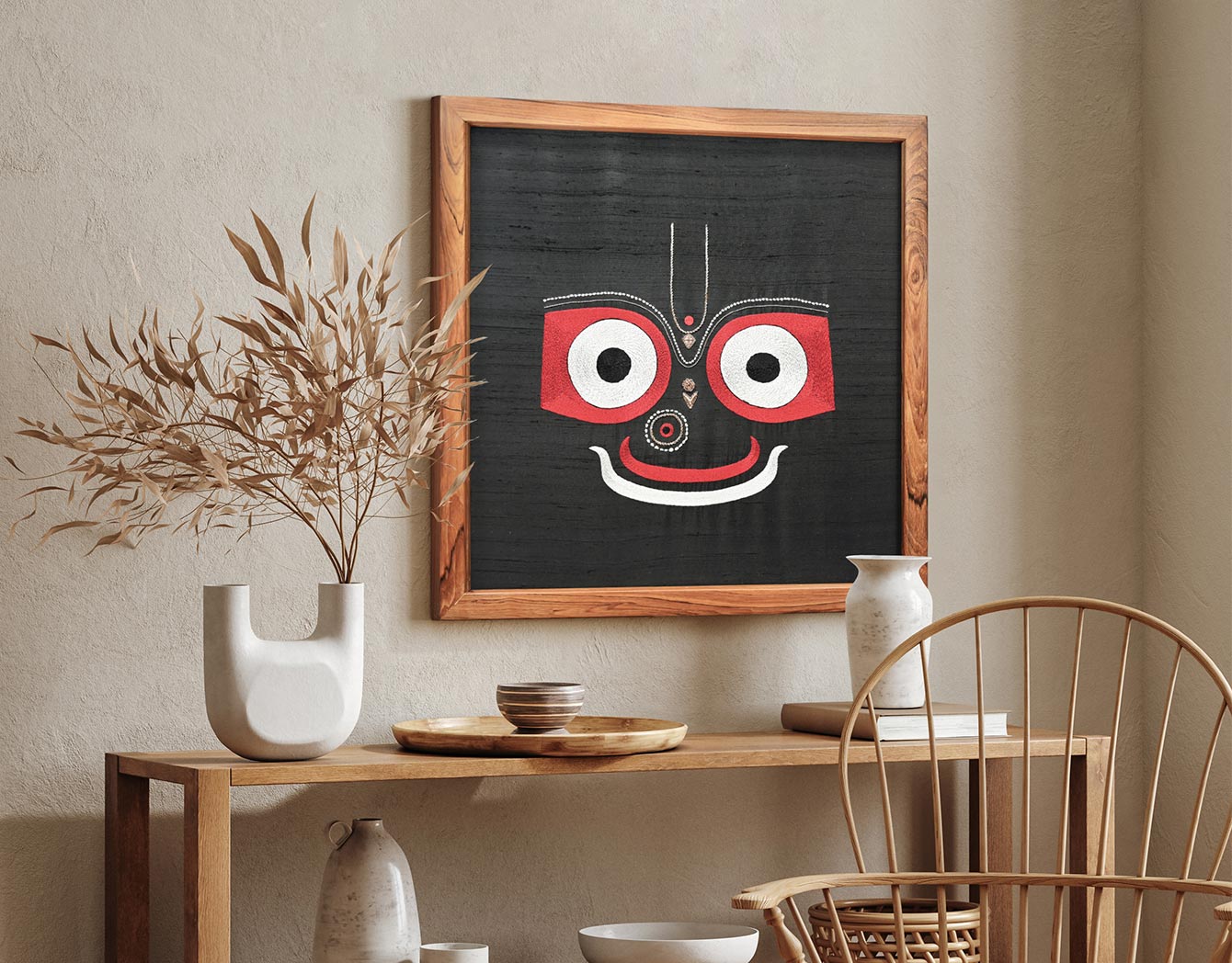 Framed artwork with a red and black face on a wall above a wooden table with decor items.