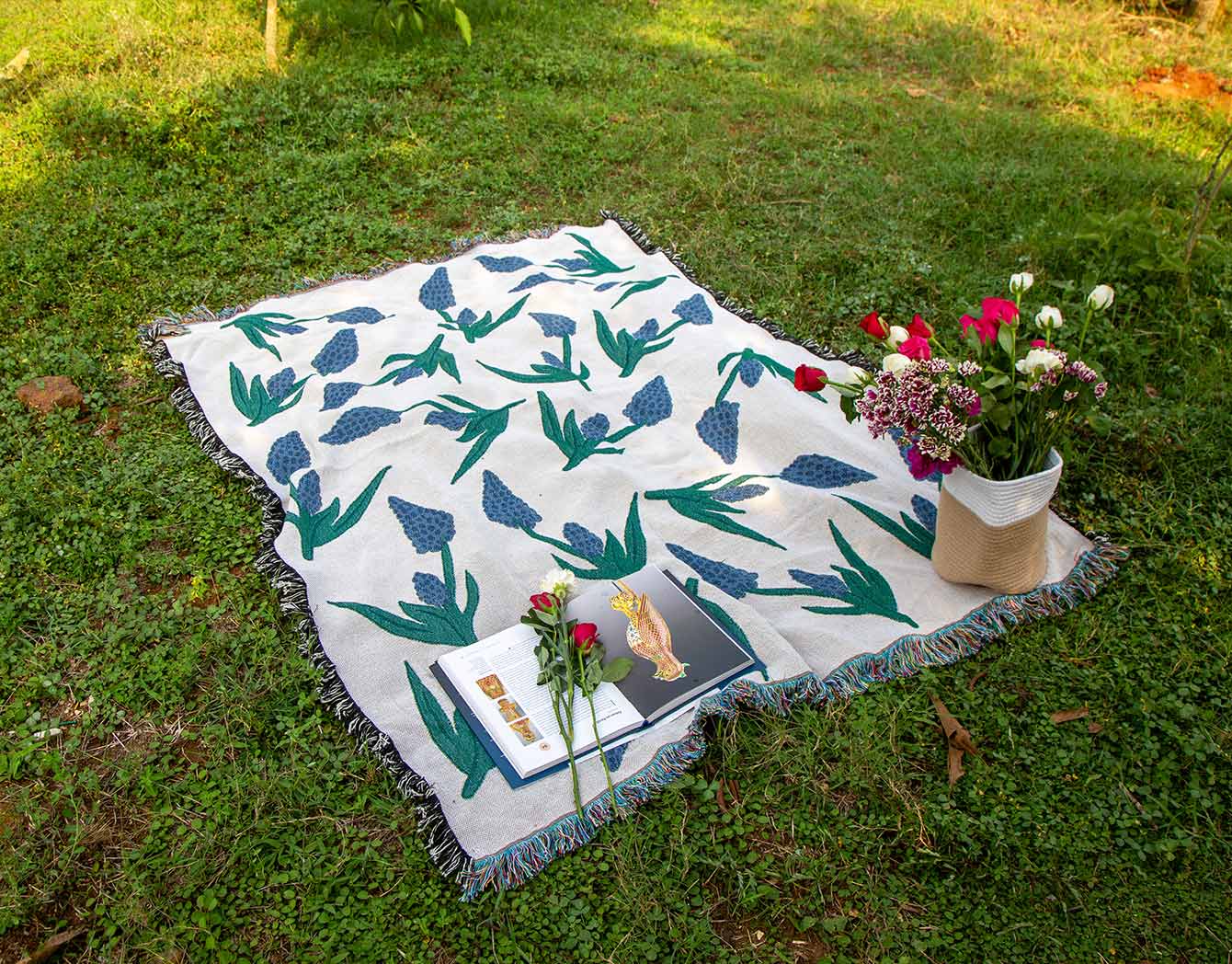 Throwblanket with floral pattern on grass, accompanied by flowers and books.