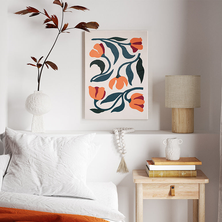 Decorative floral painting on a wall above a bed with a lamp and side table.
