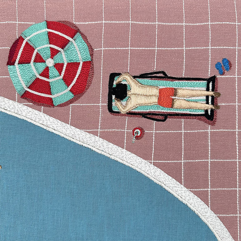 Embroidered design of a person lying on a beach with a colorful umbrella and blue sky.