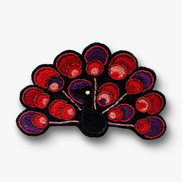 Silk-thread red peacock brooch with purple accents on a white background