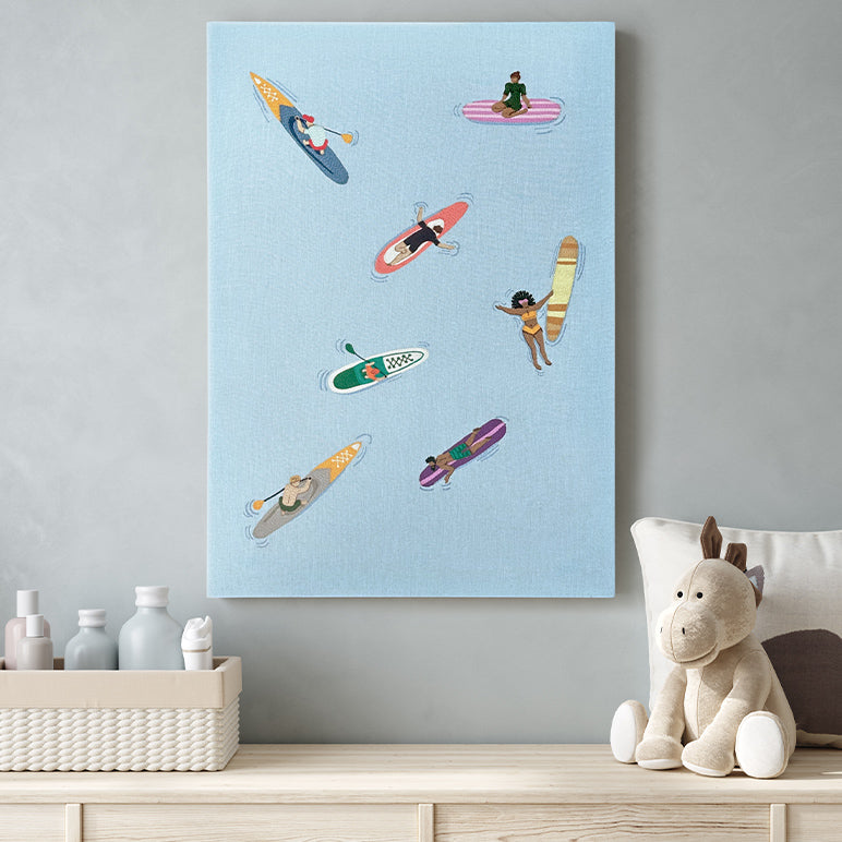 Modern wall art with colorful embroidery of people on surfboards and paddle boards hanging on a wall