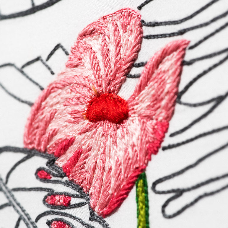 Close-up of an embroidered pink flower with a red center on a white background.