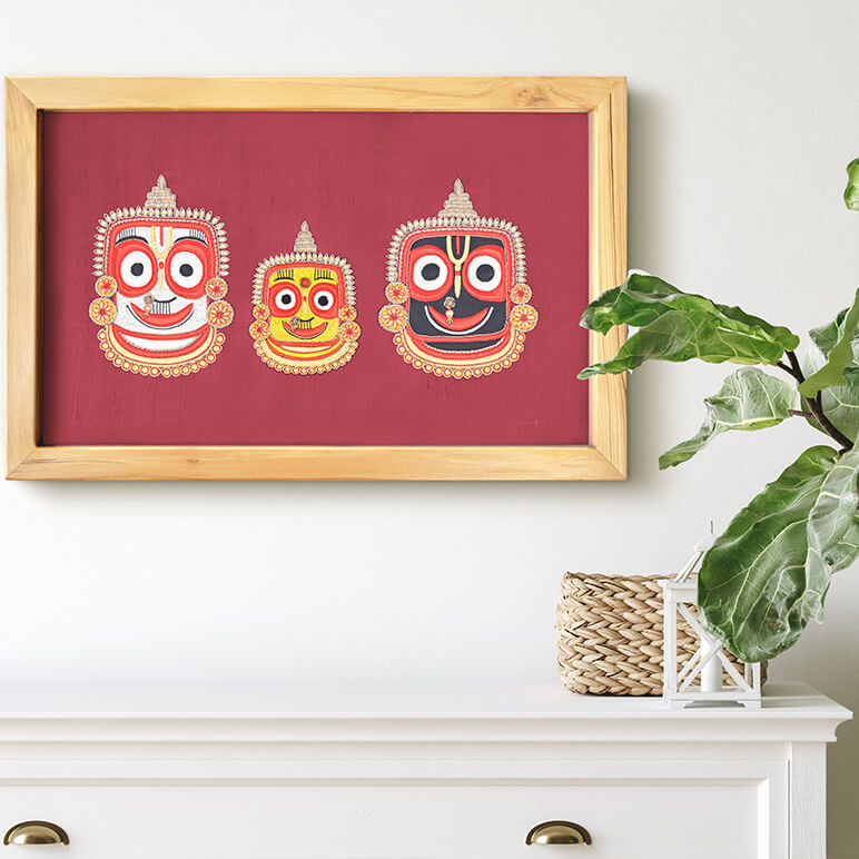 Framed artwork with three colorful faces on a red background, displayed on a white wall above a white cabinet.