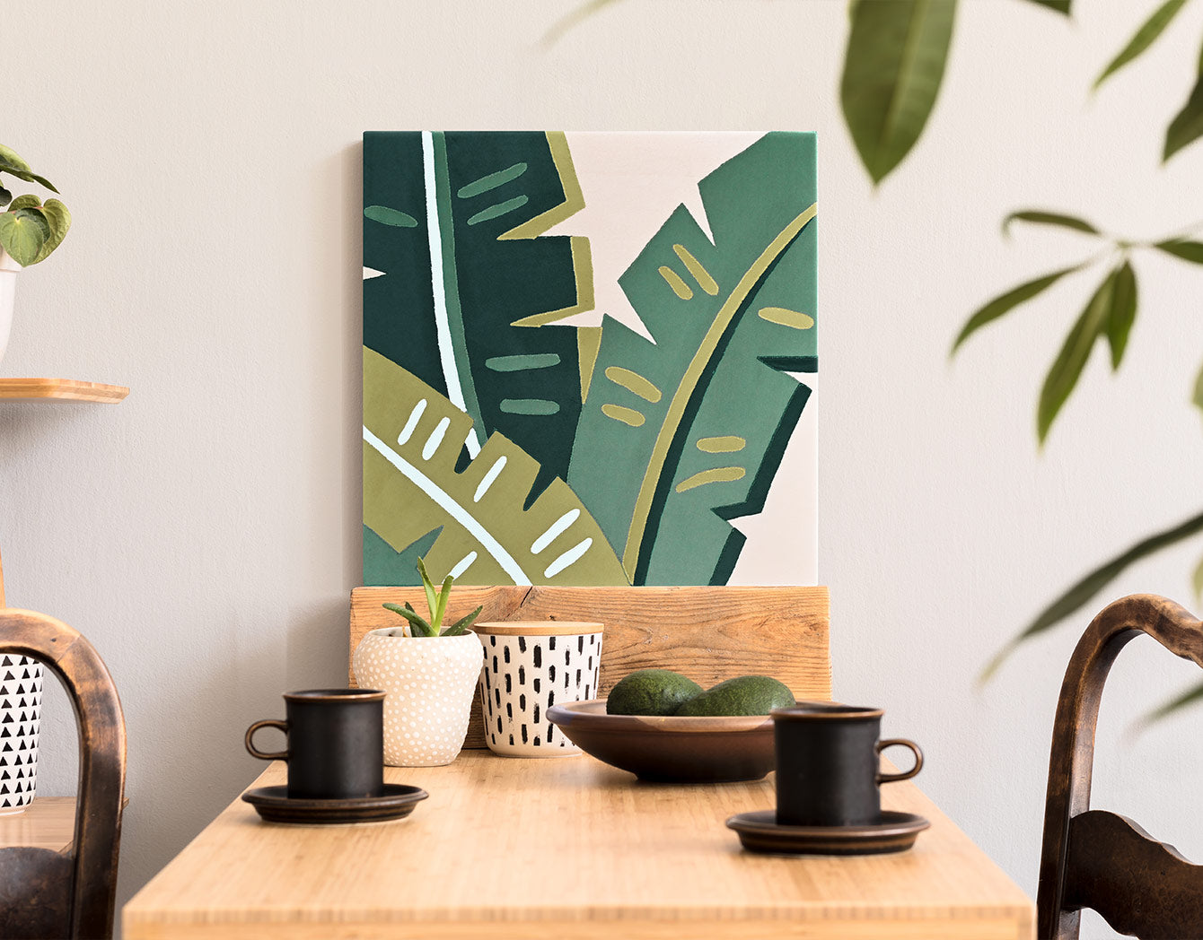 Decorative plant wall art above a wooden table with cups and a bowl.
