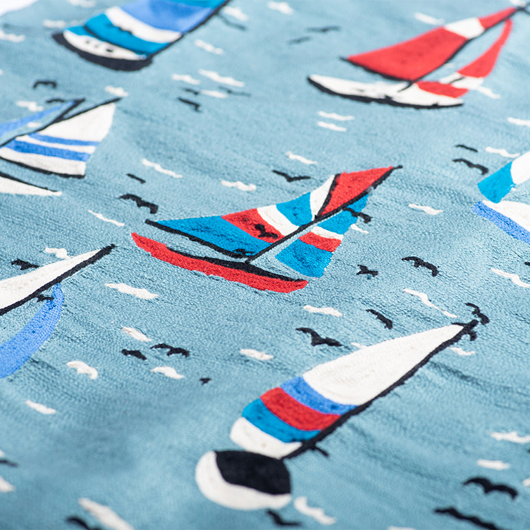 Close-up of A Summer Sail sailboat wall hanging—hand-embroidered tapestry with colorful boats on a blue sea, white wave stitches, and tiny flying birds.