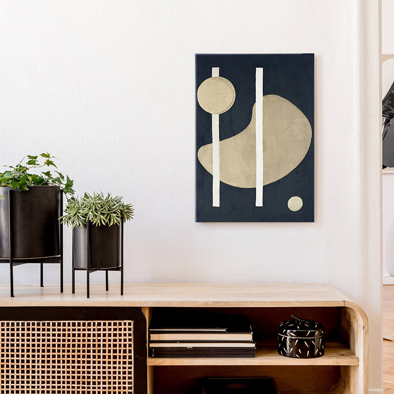 Abstract art piece on a wall above a wooden shelf with plants and books.