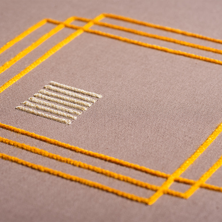 Embroidery with yellow lines and a geometric pattern on a brown background