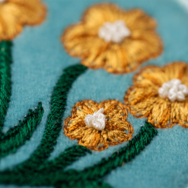 Close-up of embroidered yellow flowers with green leaves on a blue background