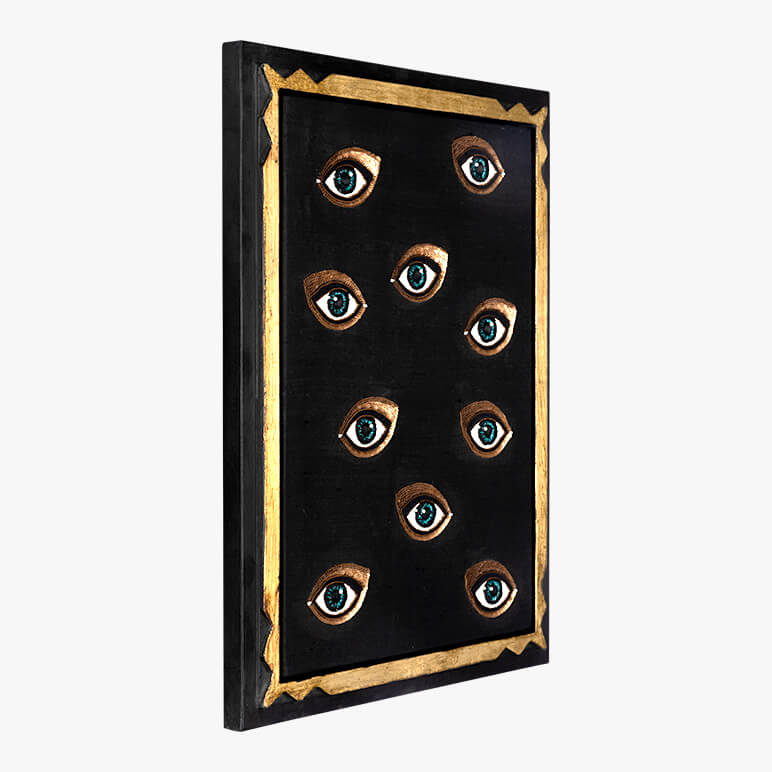 Side angle view of a decorative wall art with eyes on a black background with gold frame