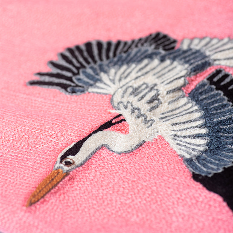Close-up of Herons nursery wall art—hand-embroidered flying heron in cream, navy and black on a bright pink ground, with textured stitches visible.