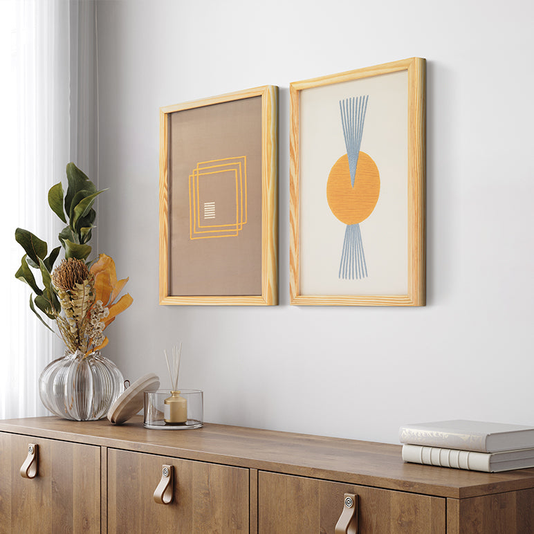 Two framed artworks on a wall above a wooden cabinet with decorative items.