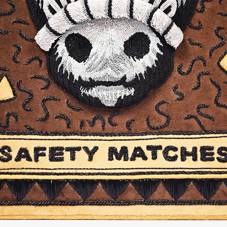 Embroidered design of a skull face on a safety matches container with brown background