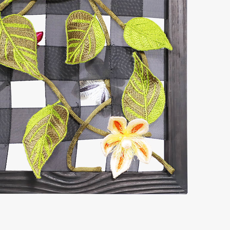 Decorative wall art with embroidered leaves and a flower on a checkered background