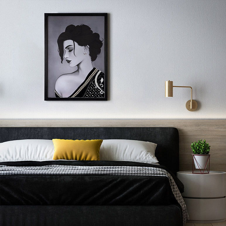 Framed artwork of a woman on a wall above a bed with decorative pillows and a nightstand.