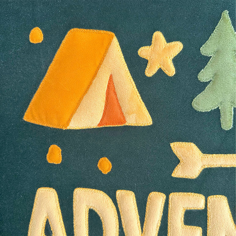 Embroidered design with a tent, star, tree, and arrow on a teal background