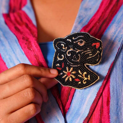 Hand holding a decorative brooch pin with a black panther on a colorful fabric background