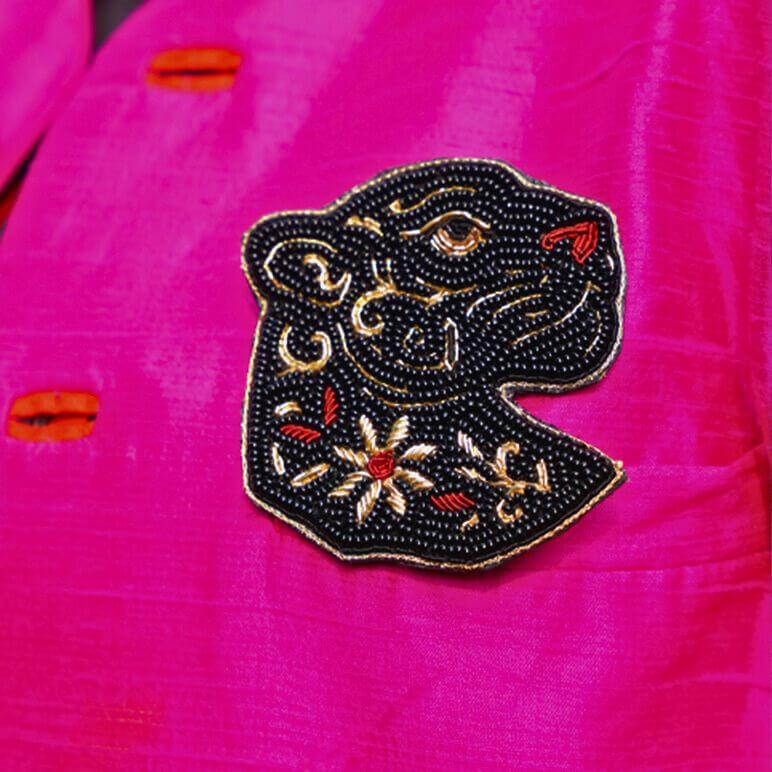 Embroidered brooch pin of a panther face on a pink fabric background