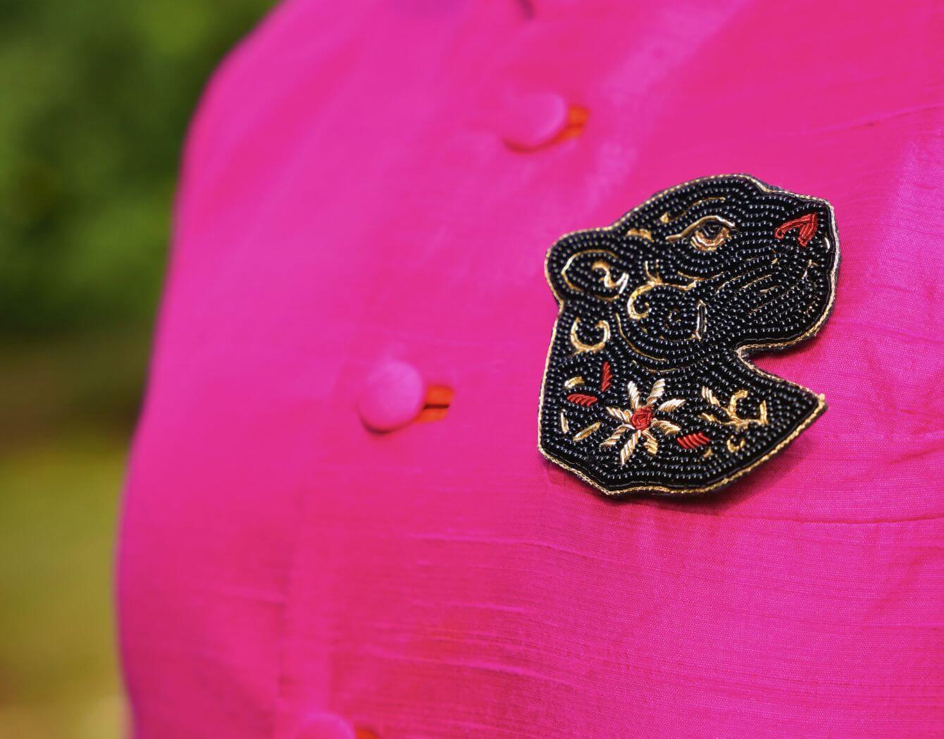 Decorative brooch featuring a black panther seen on a pink jacket with a blurred green background