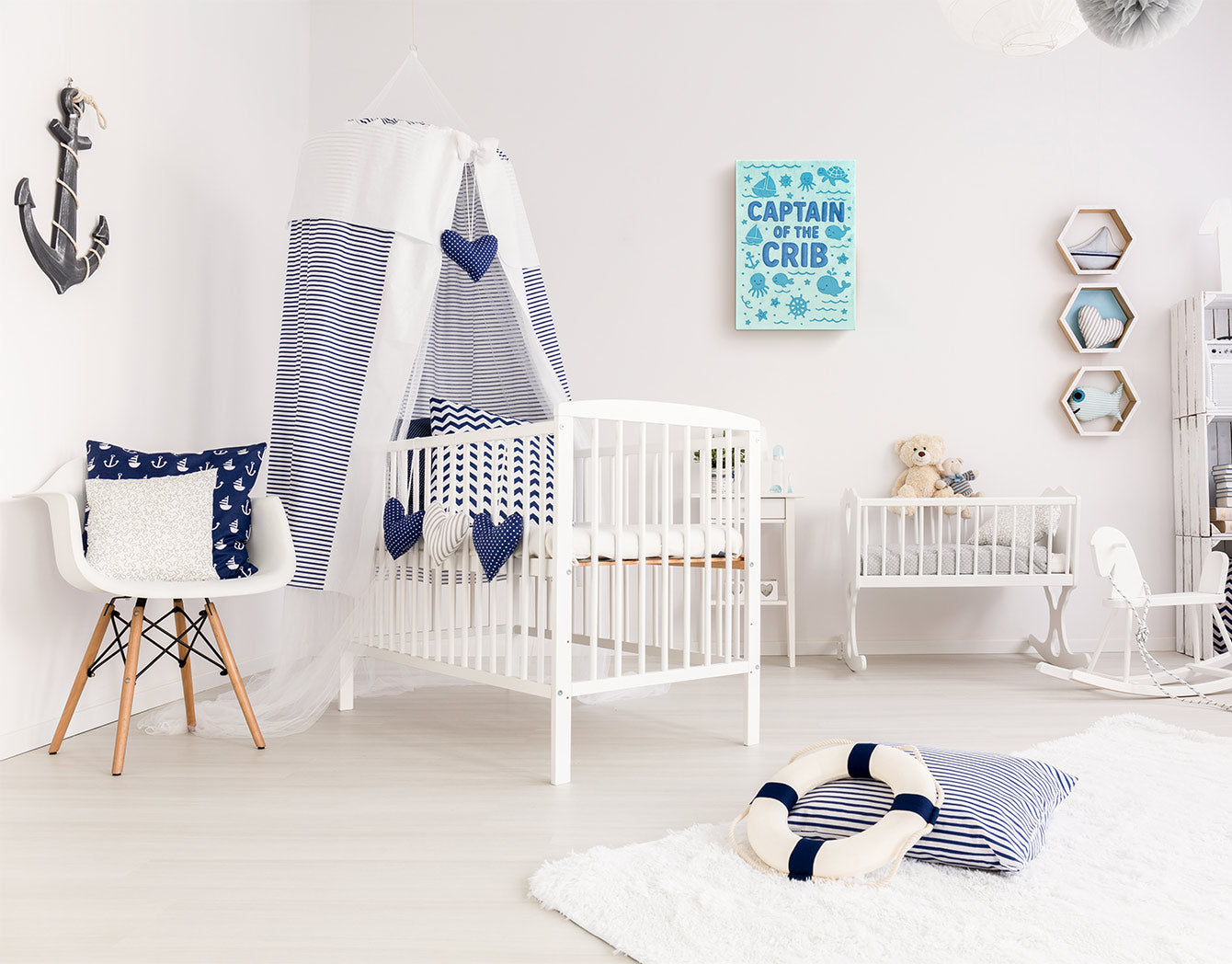 Nursery room with white crib, decorative pillows, and an embroidered textile wall art in blue nautical theme