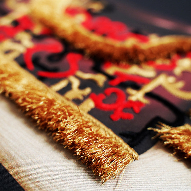 Decorative item with gold tassels and red and black patterns on a textured surface