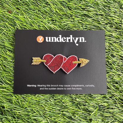 Brooch with two interlocking hearts and an arrow on a black card with &