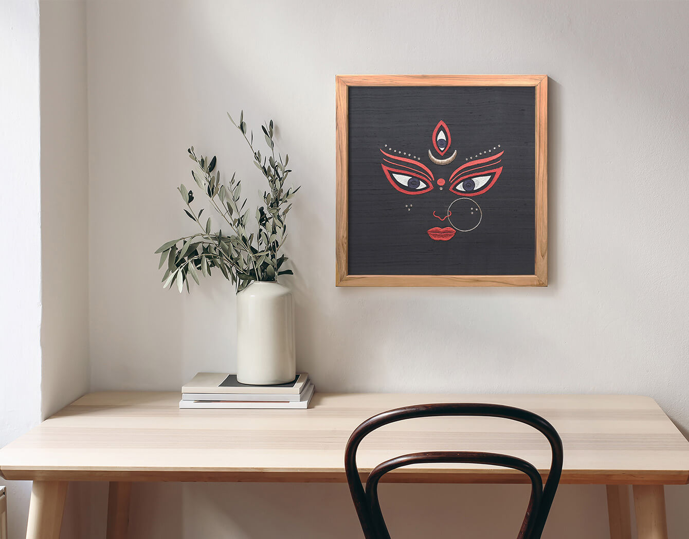 Framed artwork of a face design on a wall above a wooden desk with a chair.