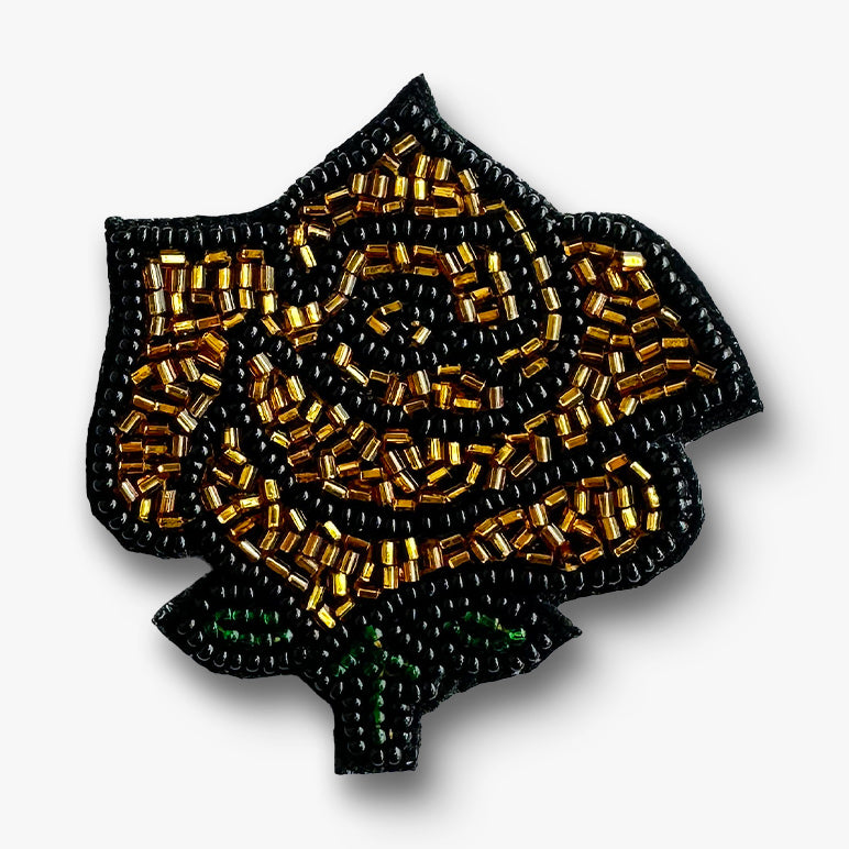 Beaded rose-shaped brooch with gold and black beads on a white background