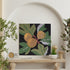 Decorative wall art with leaves and fruits on a black background, displayed in a room with plants and a clock.
