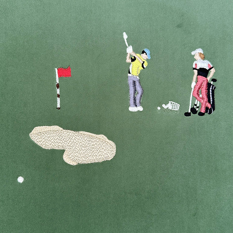 Embroidered design of a golf course with two players and a flag on a green background