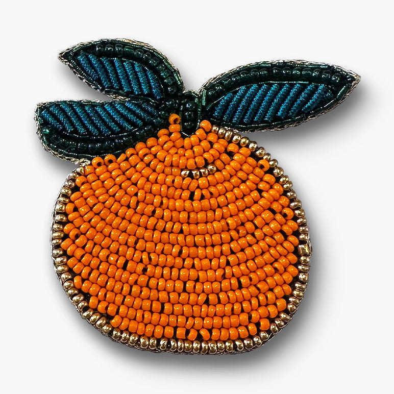 Decorative handmade beaded orange fruit with green leaves brooch pin on a white background