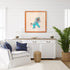 Living room with white walls, a white sofa with blue pillows, a wooden sideboard, and a framed artwork of a blue creature.