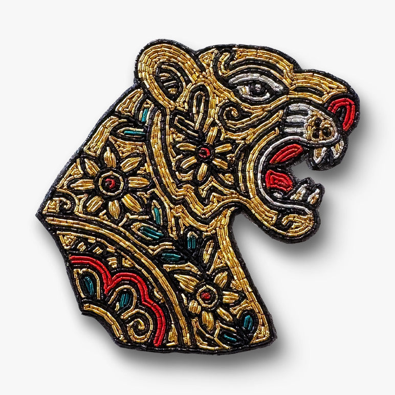 Decorative hand-embroidered Gold tiger head brooch with red and green color on a white background.