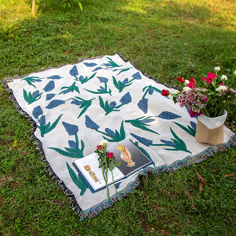 Floral-patterned picnic blanket on grass with flowers and books.