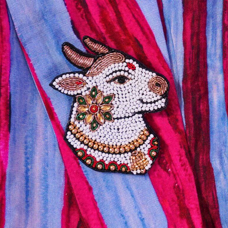 Decorative brooch pin showing divine Nandi with jewelry on a colorful fabric background