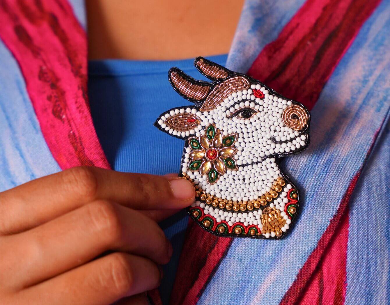 Decorative Nandi brooch pin seen on a colorful blazer with a hand touching it