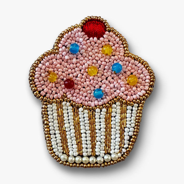 Decorative pink cupcake-shaped brooch pin with beads on a white background