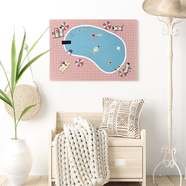Framed artwork of a pool scene with people on a pink checkered background, displayed above a wooden bench with a blanket and pillow.