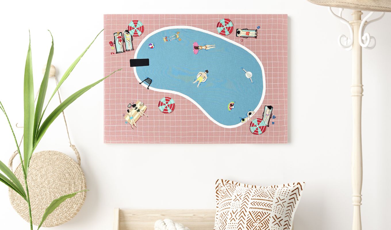 Decorative wall art of a pool scene with people on a pink grid background, placed on a white surface.