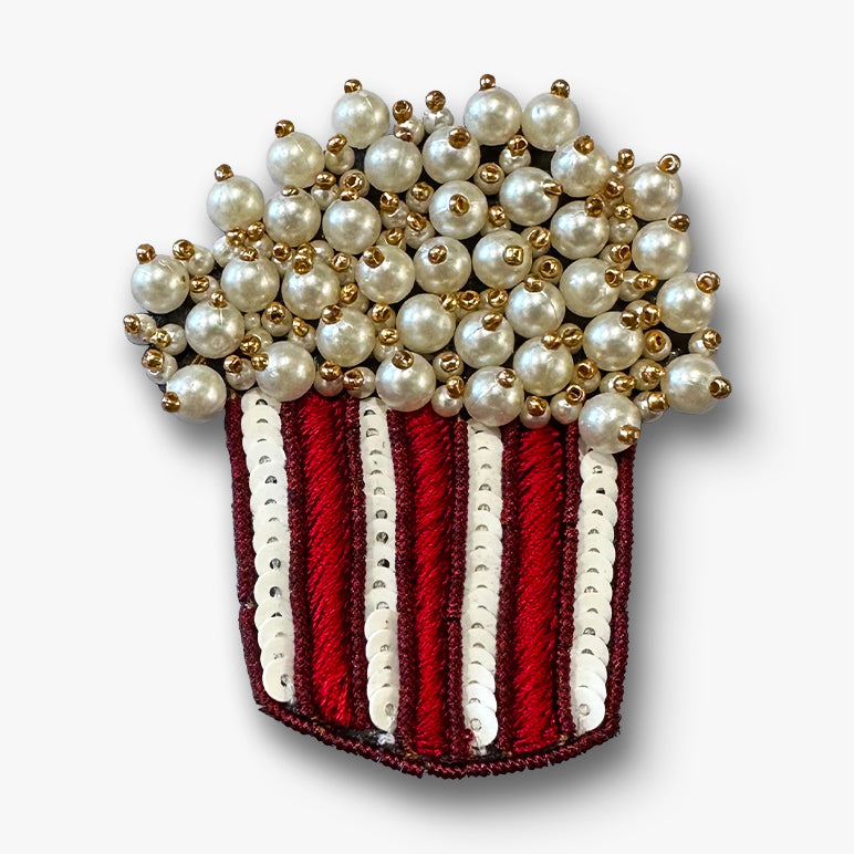 Pearl-topped popcorn bucket brooch pin with red-and-white sequined stripes on a white background