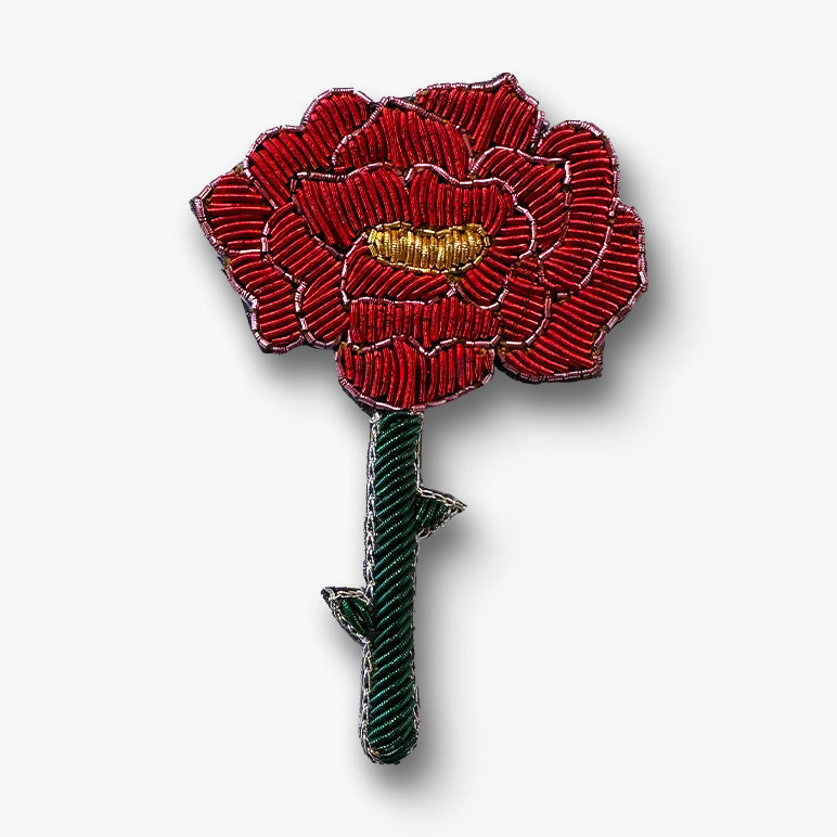 Red flower brooch pin with gold centre and green stem on a white background