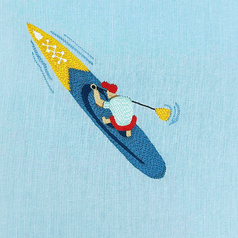 Embroidered design of a penguin in a kayak on a light blue fabric background